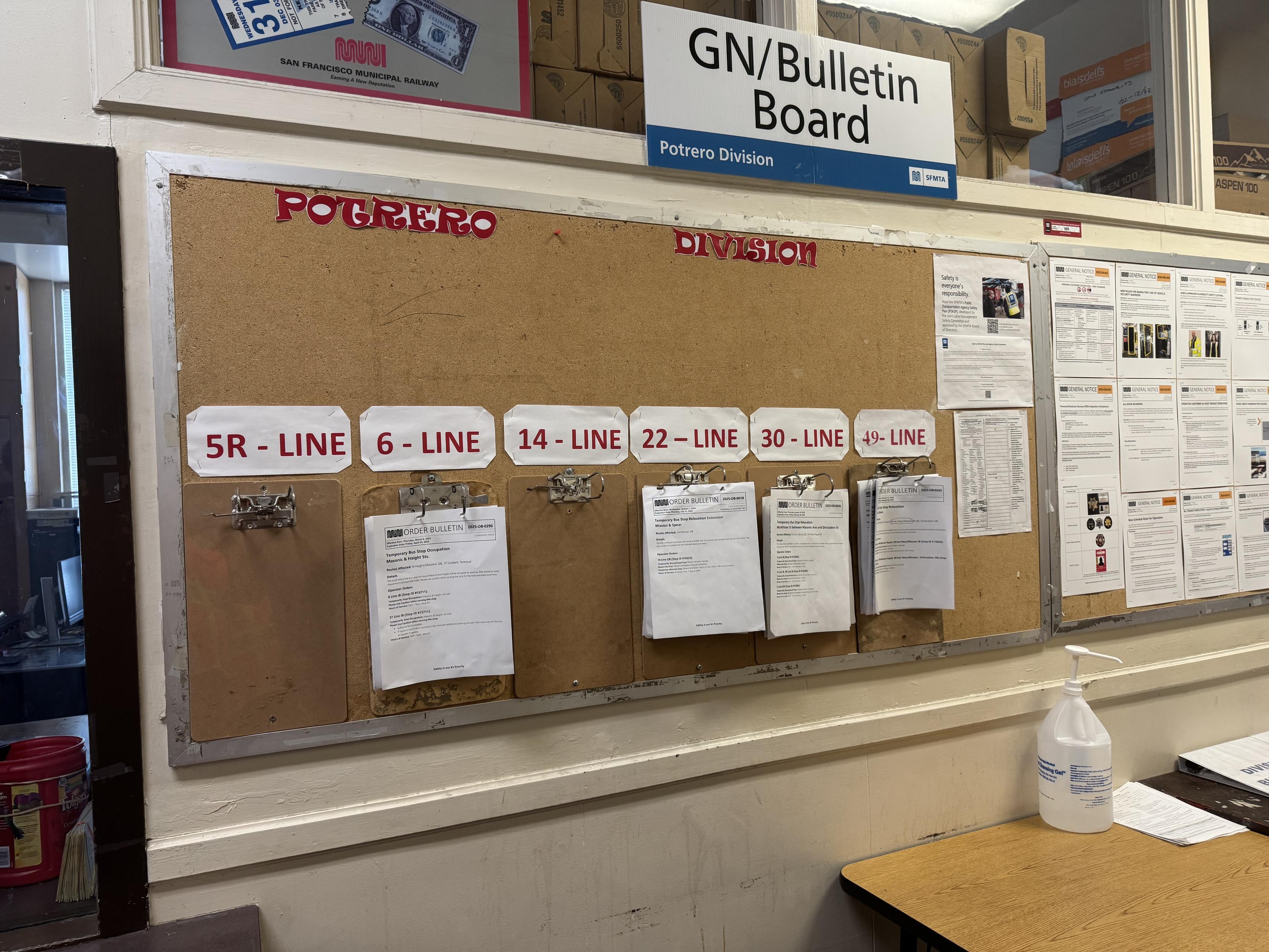 A bulletin board of notices for route operators of the routs that are homed in this staion. Hand cut red letters are taped to the top which say POTRERO STATIONclipboards for six lines are mounted on the board under white paper with red lettering indicating the line they correspond do.From left to right:5R - LINE, 6 - LINE, 14 - LINE, 22 - LINE, 30 - LINE, 49 - LINEI take the 14 and 49 very frequently, I used to take the 22 less frequently and now infrequently but it is a critical line to me when I need. Love to see this!