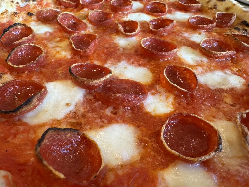macro close up of the pepperoni pizza. the pepperoni is cupped and the cheese is melted in circles, making an overlapping polka dot effect over the red tomato sauce.