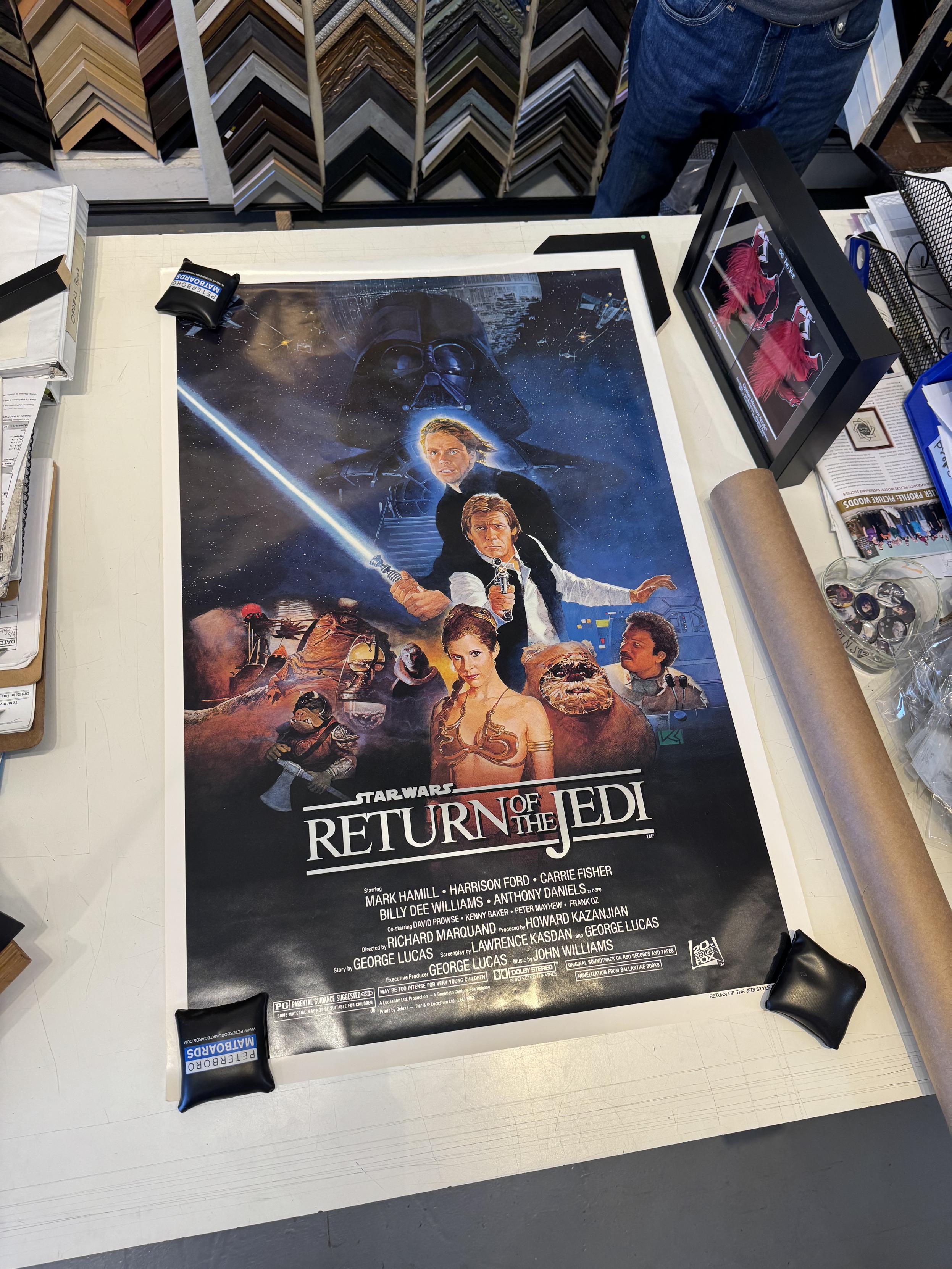 a giant table-covering poster labeled “STAR WARS REURN OF THE JEDI SERIES B ONE SHEET”which had been stored rolled, never folded, and in mind condition, I assume for 42 years (circa 1983) but maybe a repro?This is one of the illustrated headshot ones with darth vader in front of the second death star top center, luke under him, han under that, and the rest of the cast horizontal below Junior and I just happened to watch this one last weekend and it is pretty hokey, but the people in the store were all pretty excited by it. 
