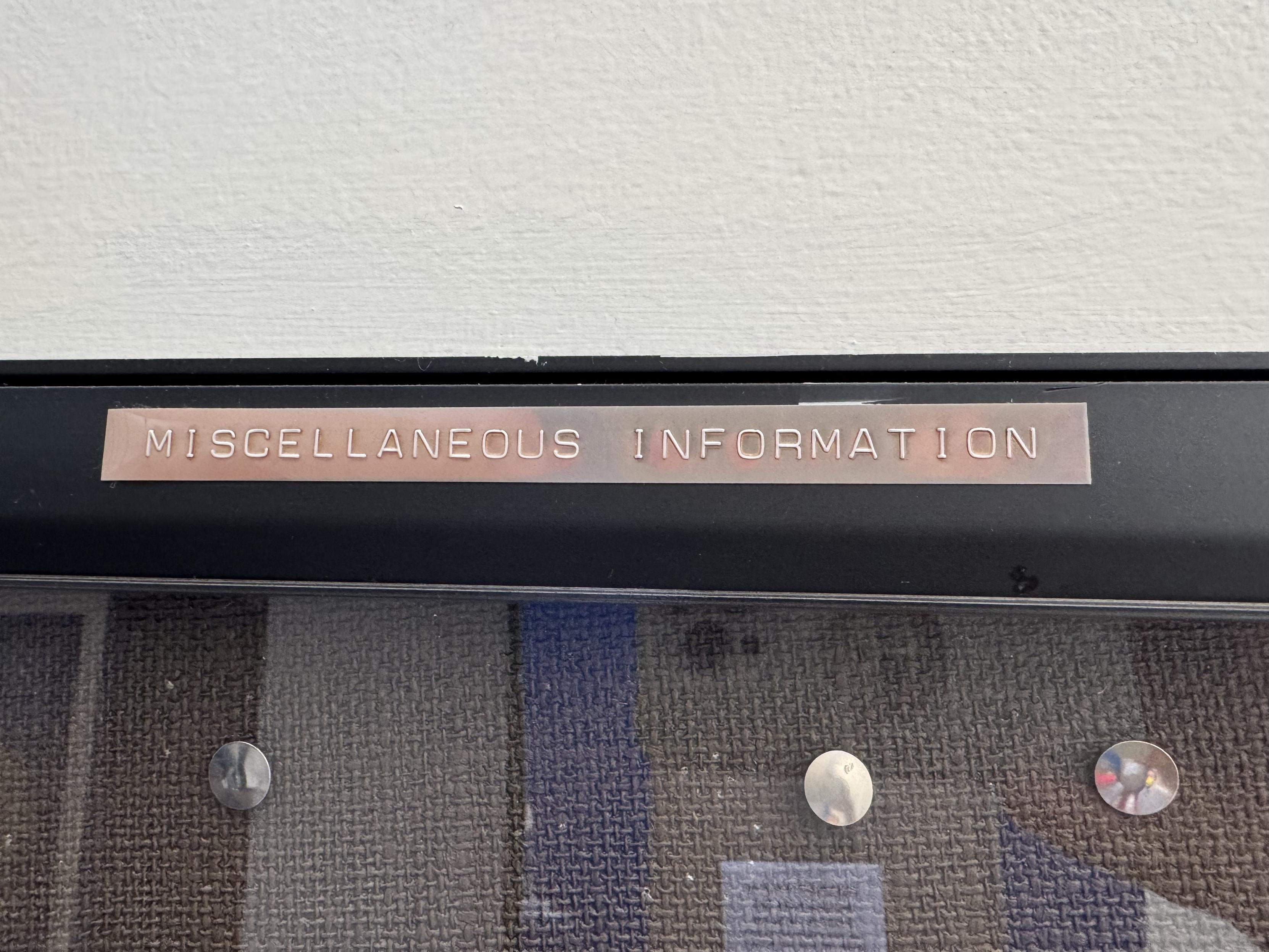 an old fashioned plastic punch letter ribbon sticker that was probably red a very long time ago which proclaims in all caps on top of a glass display case at the post office: MISCELLANEOUS INFORMATION