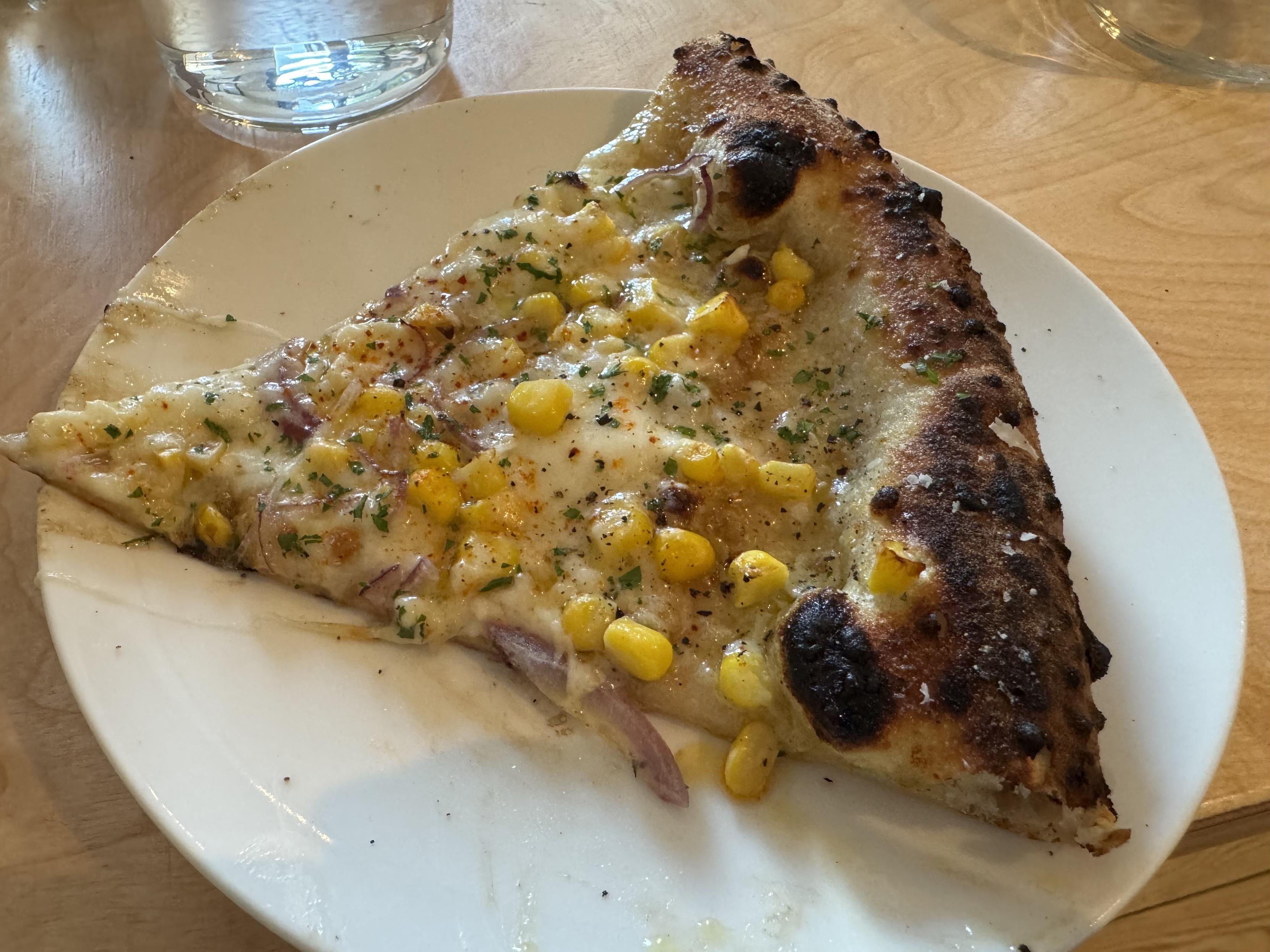 a single slice of neapolitan pizza topped with mozz, sweet corn, and a few very tiny, thin red onion slices. I think it also has oregano flaks and chili powder and maldon on top