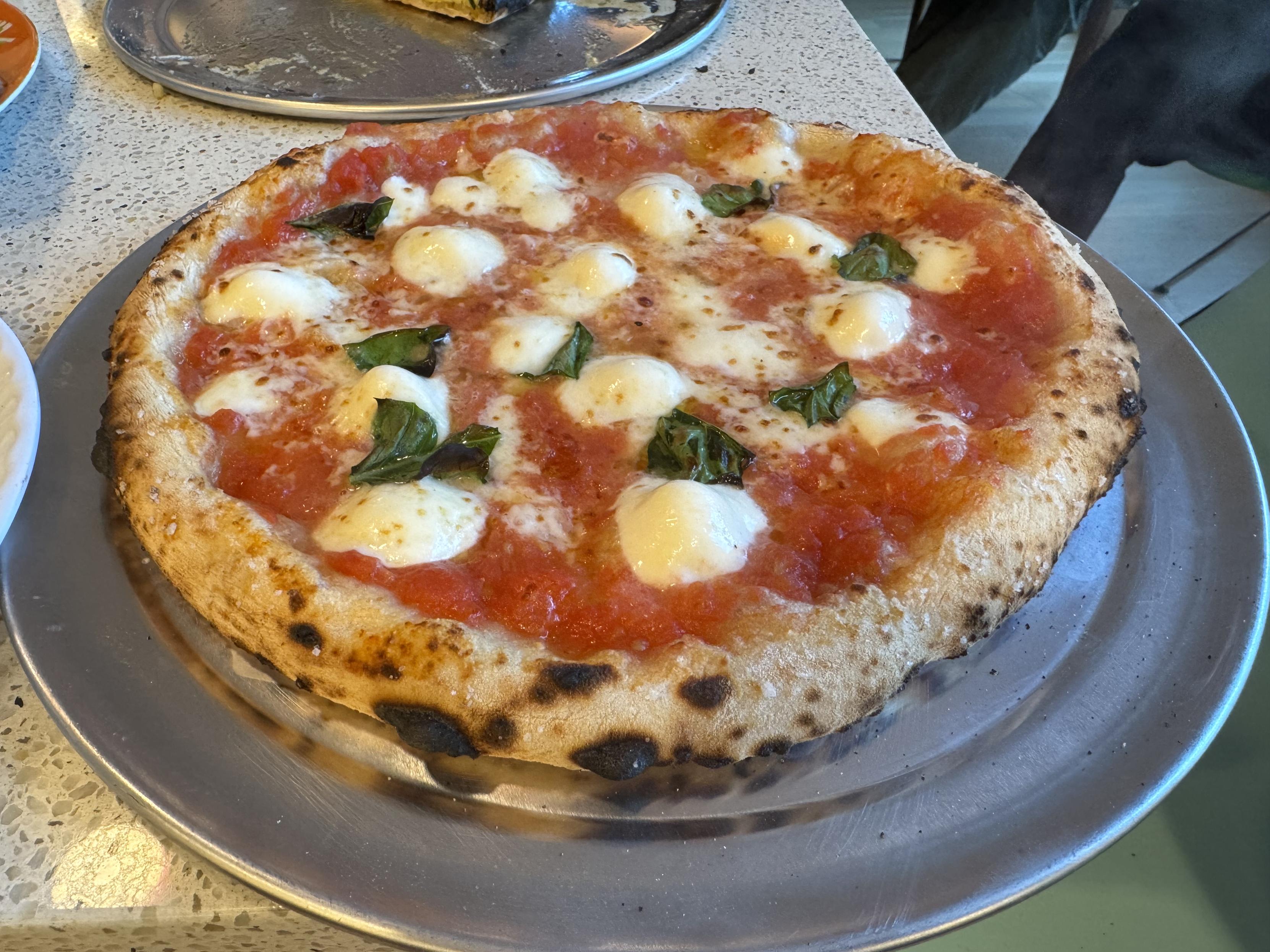 a standard neapolitan margherita on a stainless steel platethe pizza is topped with san marzano tomato (I open a can, pour off half of the tomato juice down the drain, dump the whole peeled tomatoes in a blender with a pinch of salt and blip it very briefly), smoked mozz, microplaned parmesan, fresh mozz, and a few tears of basil leaf. I salted the corniccione with fleur de sel.