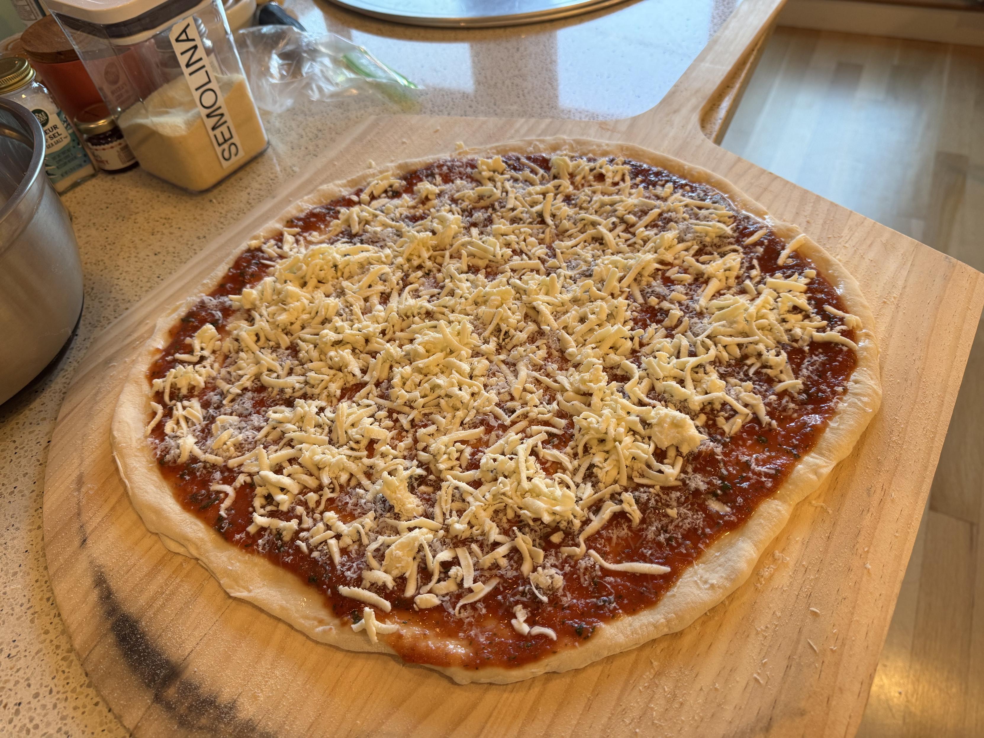 an 18” NY style pizza on a wooden peel, prior to baking. I make NY style sauce w/ san marzanos, salt, sugar, half a clove of garlic, and a dozen basil leafs in a blender. the pizza is topped with parm and low moisture mozz