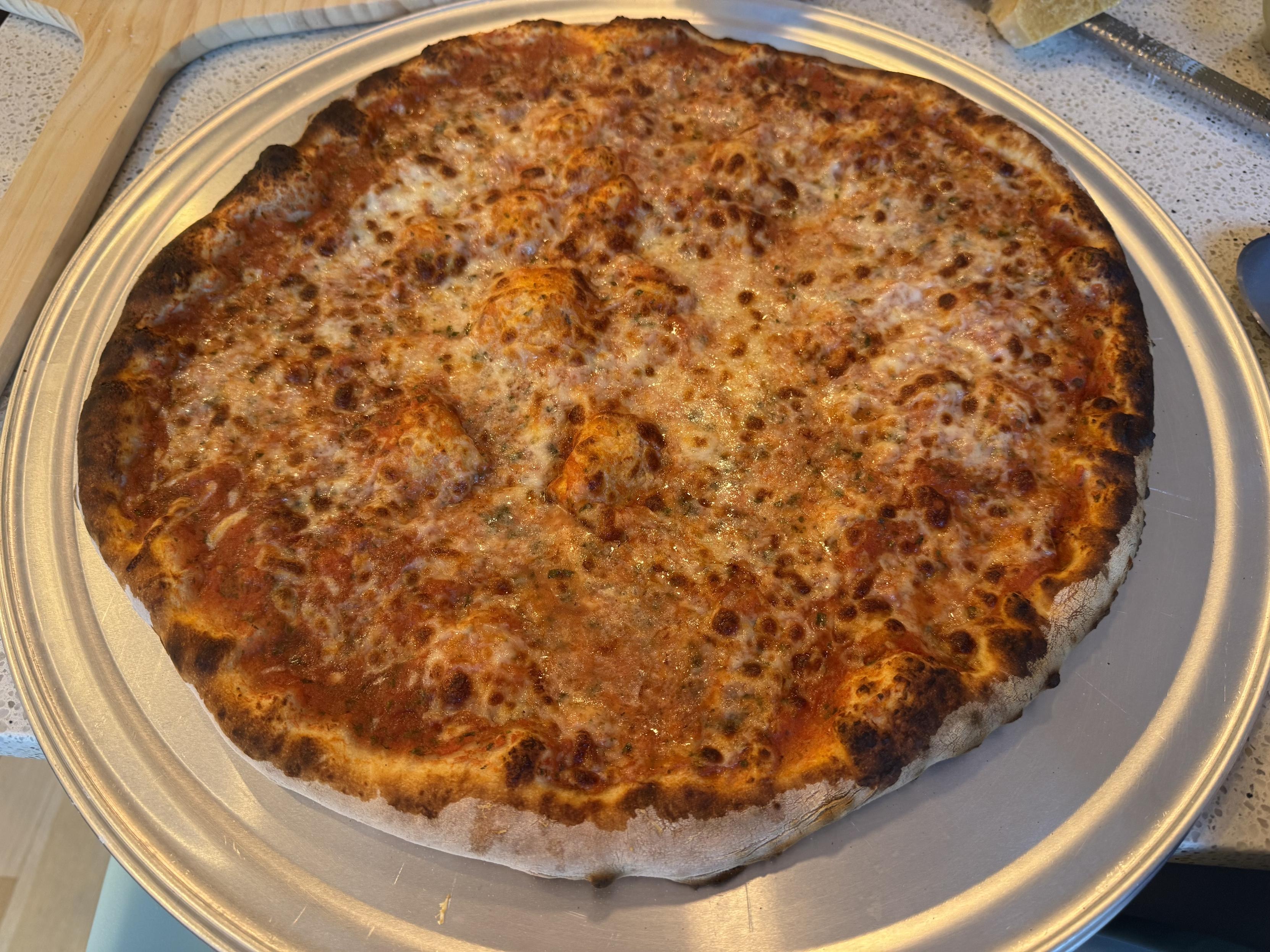 a just-baked 18” NY style pizza on a steel platethe pizza is topped with tomato sauce, parm and low moisture mozz