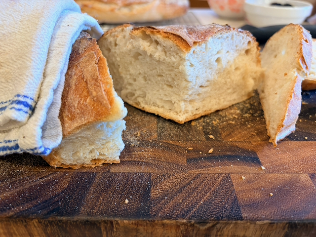 A few cuttings of the bread from the side, exposing the crumb, with a kitchen towel resting on the left side which I used to keep from burning my hand while I sawed through the still-hot loaf.