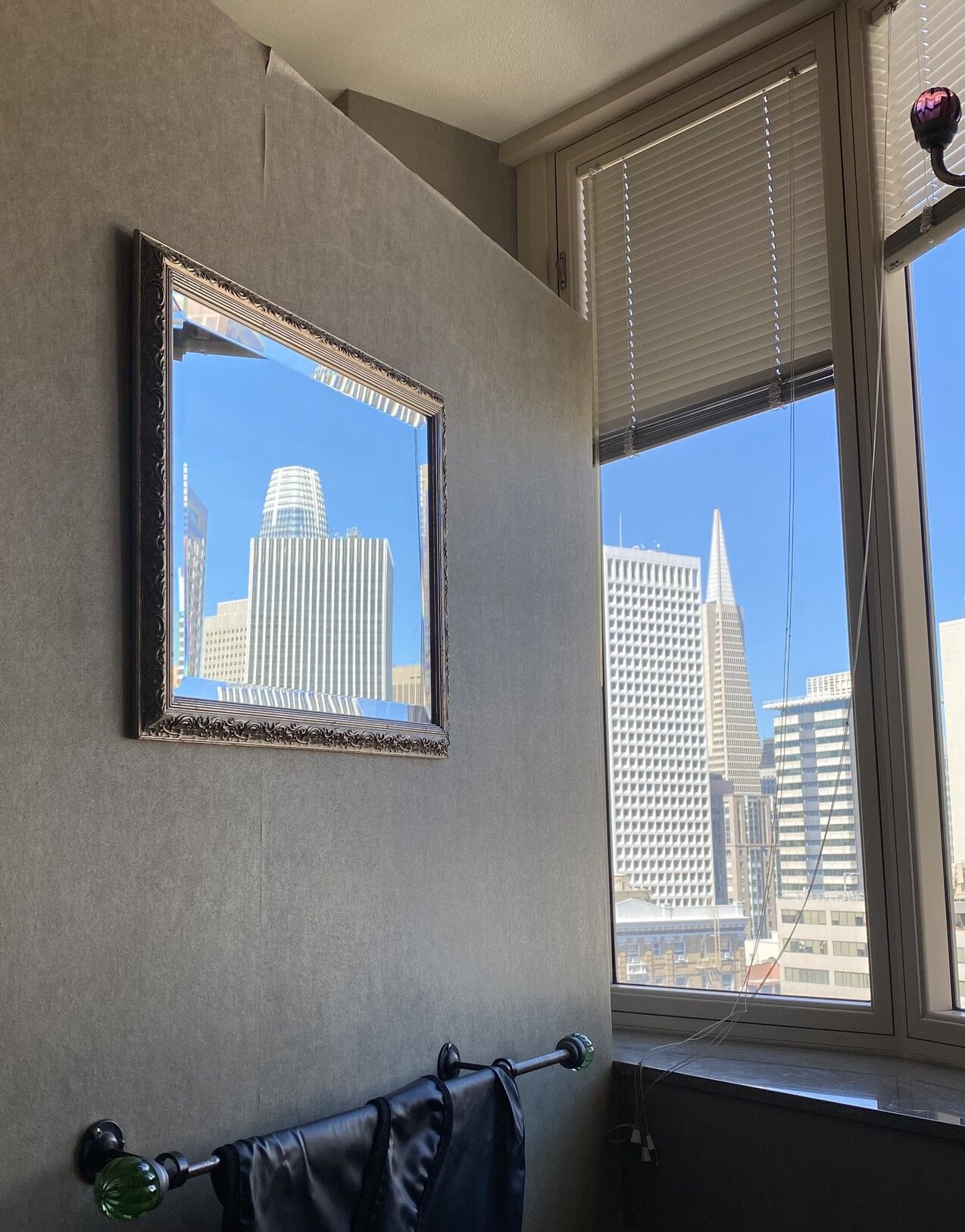 photograph of an open window with the Transamerica building in the center, through which a mirror on a perpendicular wall shows a view of the top of the salesforce tower (which needs a better name imo)one of those lead blankets they use for x-rays hands on a rack below the mirrormy astro teacher in high school used to lol about those x-ray bibs, apparently the radiation you could get hit with by an xray machine ist like, not even close to what you get hit with taking any airline flight? i should look that up