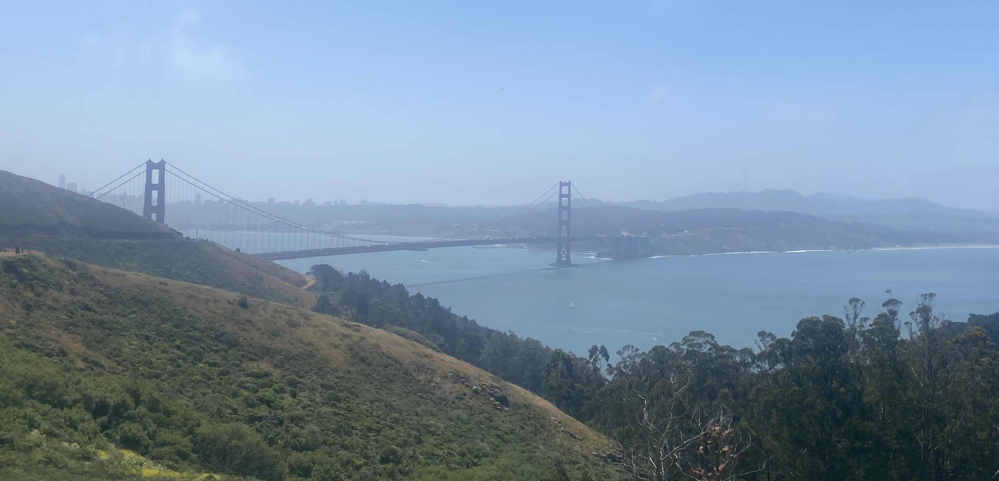 the west side of the golden gate bridge over the hills and far way away on a sunny but hazy day from the trail head, not seen again the rest of the hikethe san francisco city skyline and sutro tower are barely visible in the haze
