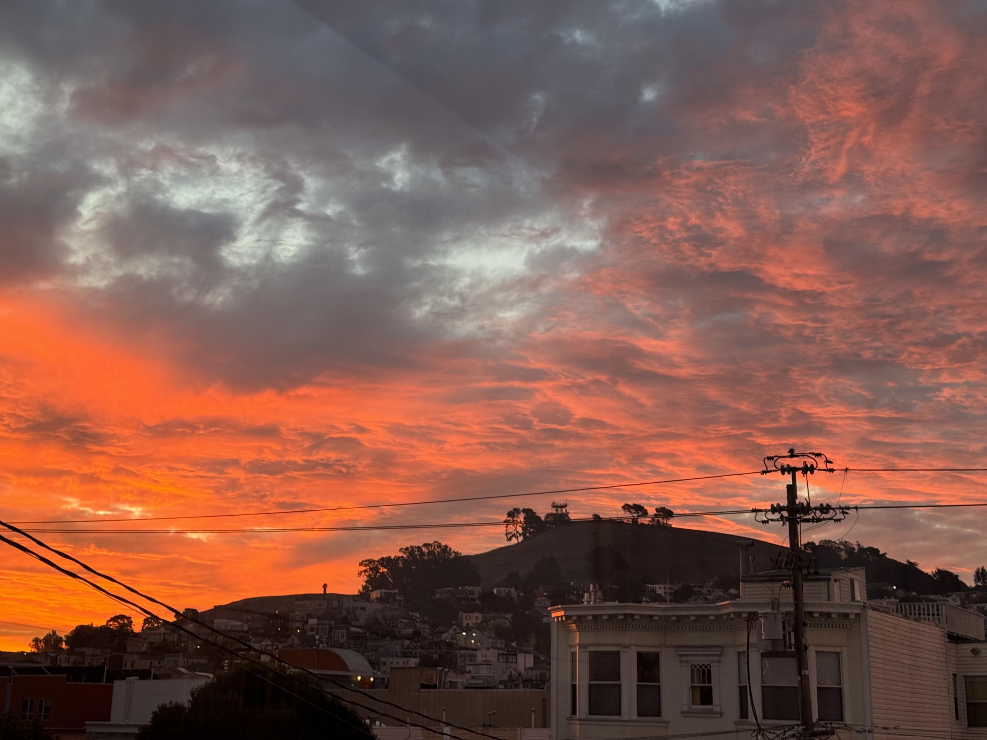 sunrise over bernal heights, the left and right, most distant bands of clouds are bright orange, the nearest high clouds are white and blue