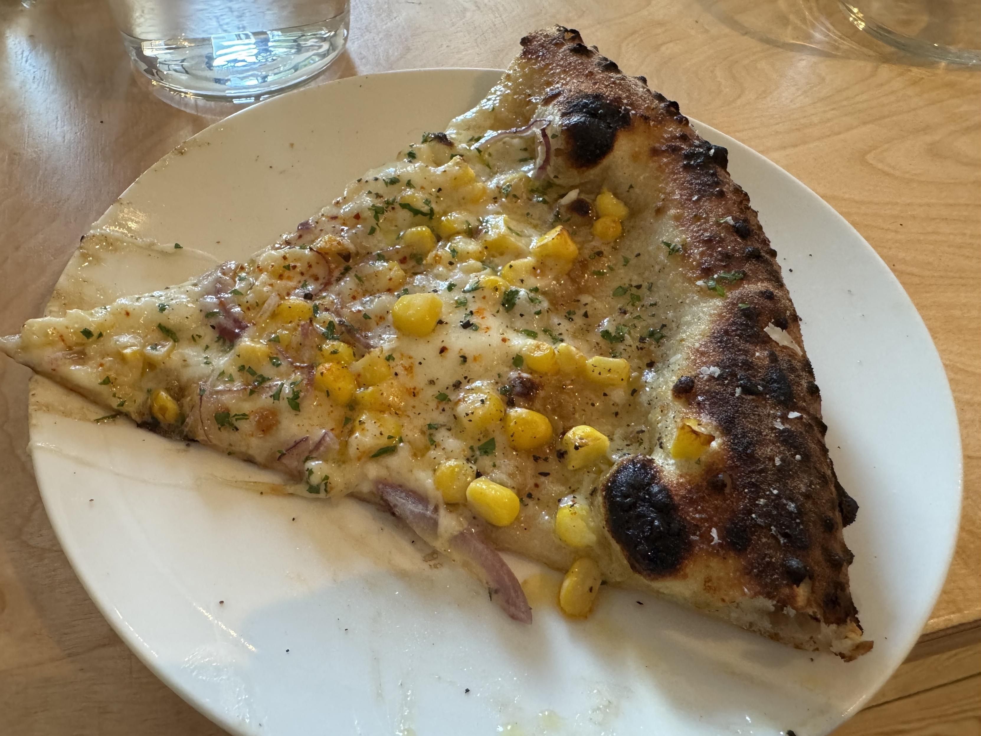 a single slice of neapolitan pizza topped with mozz, sweet corn, and a few very tiny, thin red onion slices. I think it also has oregano flaks and chili powder and maldon on top
